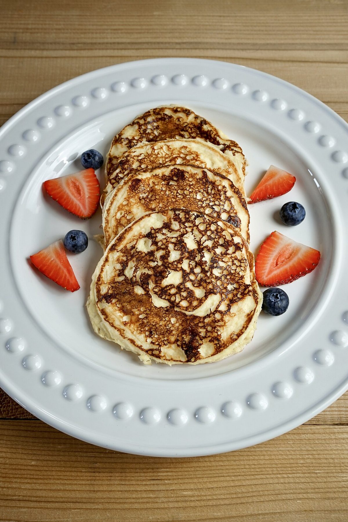 A stack of golden low-carb pancakes with strawberries and blueberries on a white plate