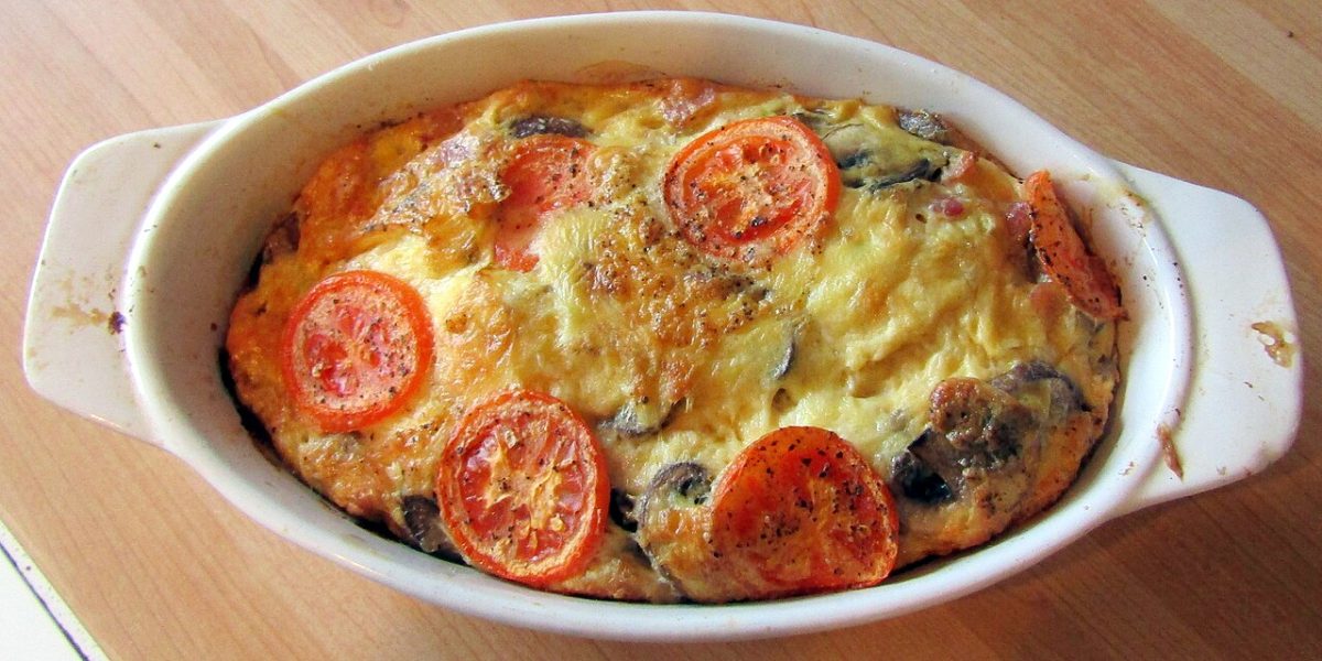 A baked bacon and mushroom frittata with tomato slices in an oval dish