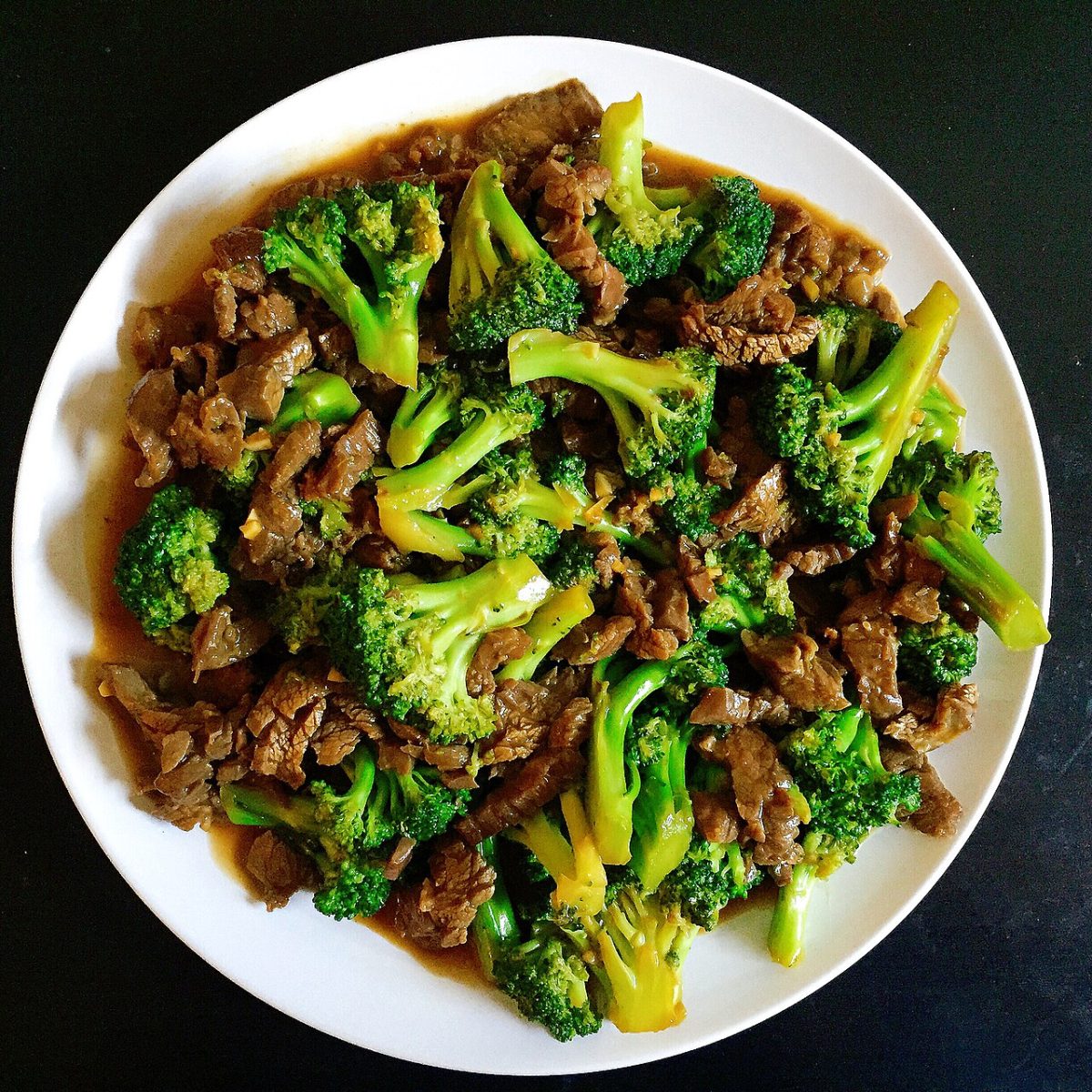 Sliced beef and bright green broccoli florets in a glossy brown sauce on a white plate