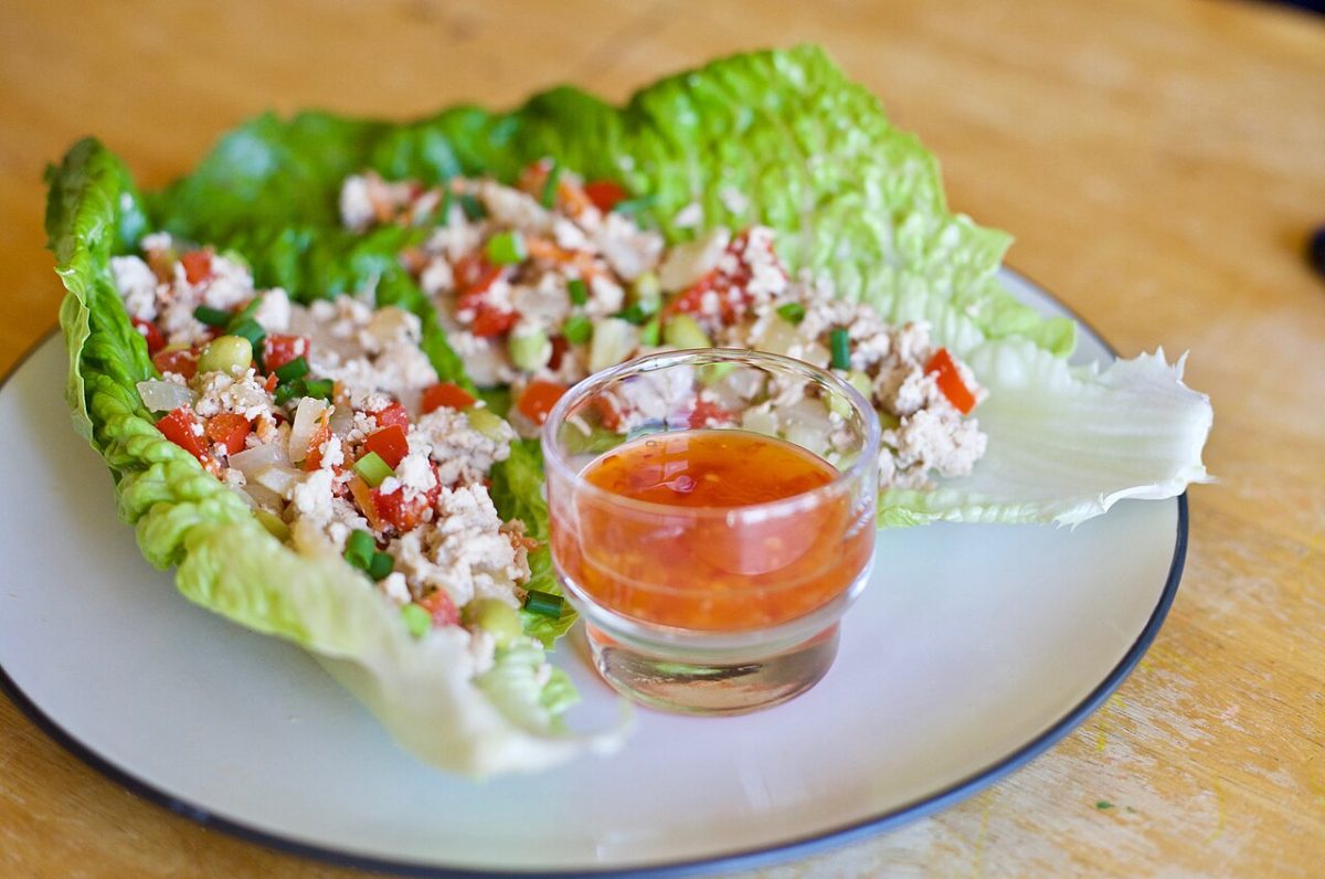 Romaine lettuce leaves filled with seasoned ground meat and diced peppers, with a small cup of sauce