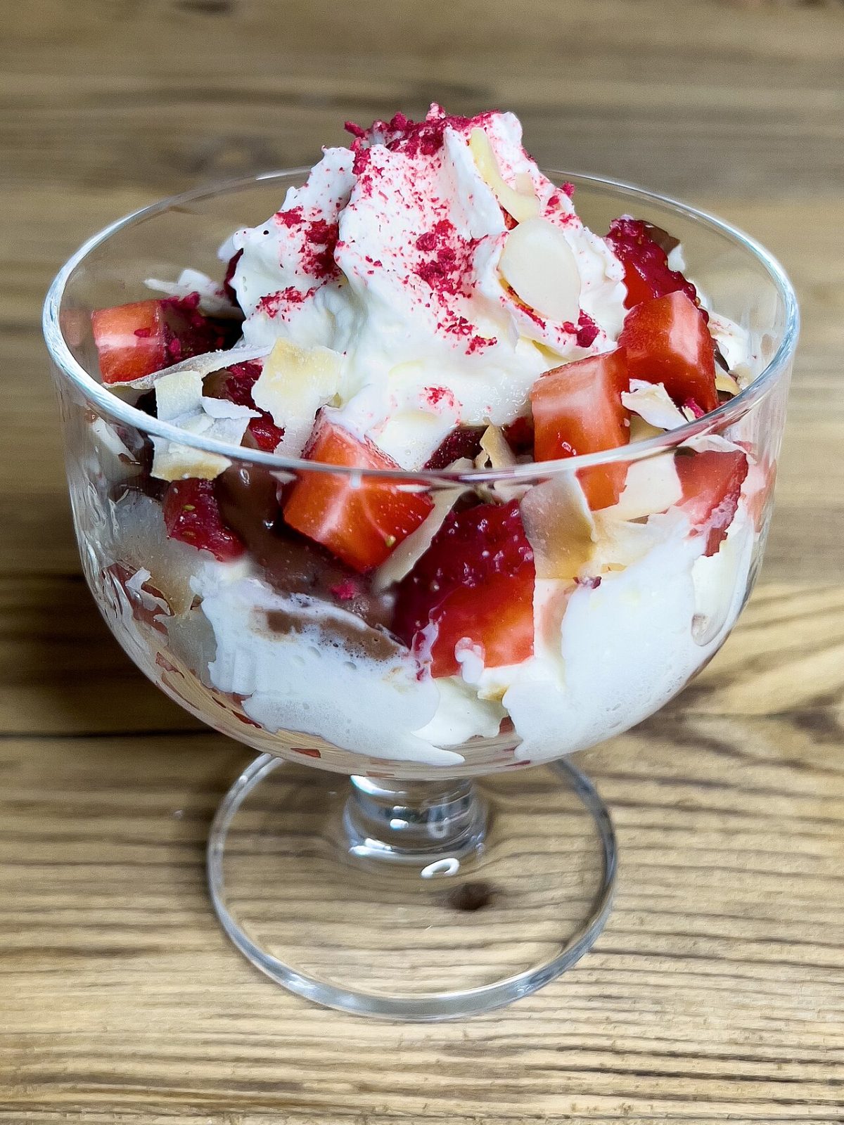 A glass cup of whipped cream with chopped strawberries and sliced almonds
