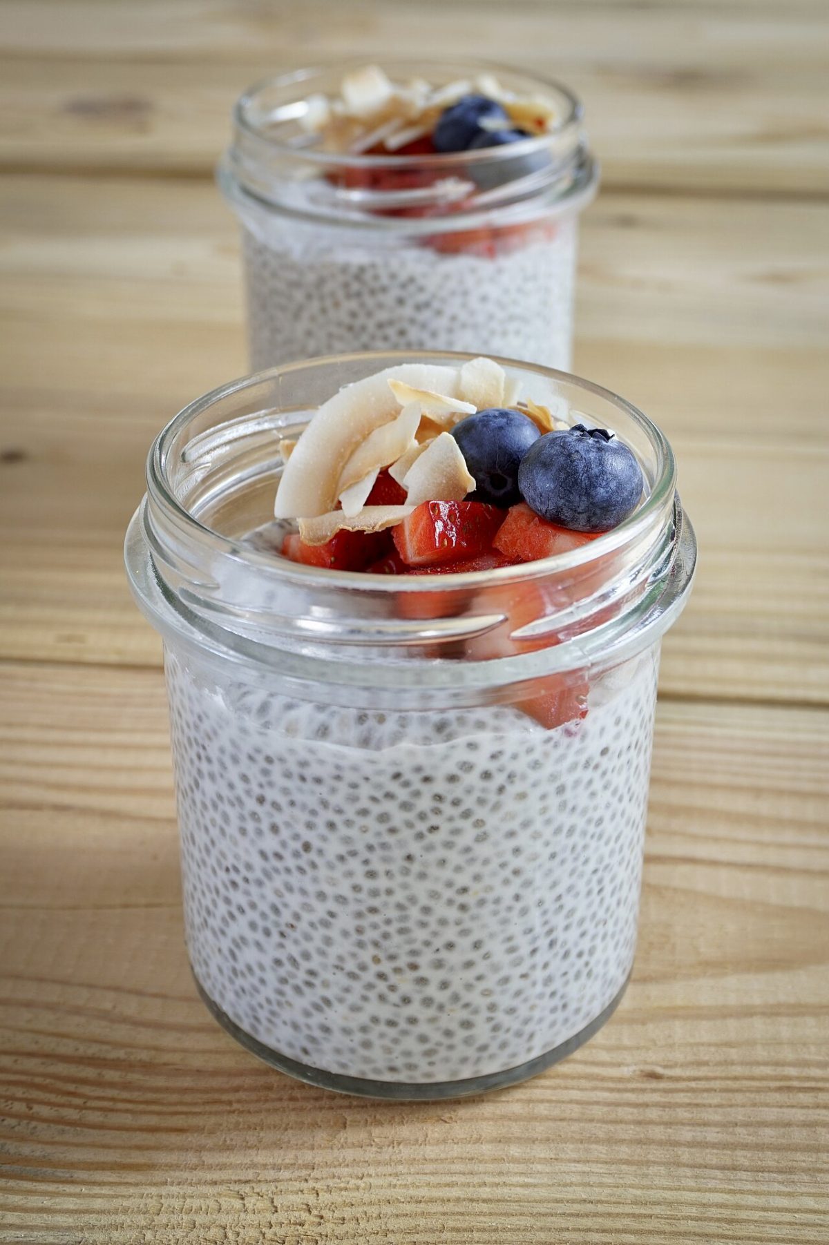 Two glass jars of chia pudding topped with berries and coconut flakes