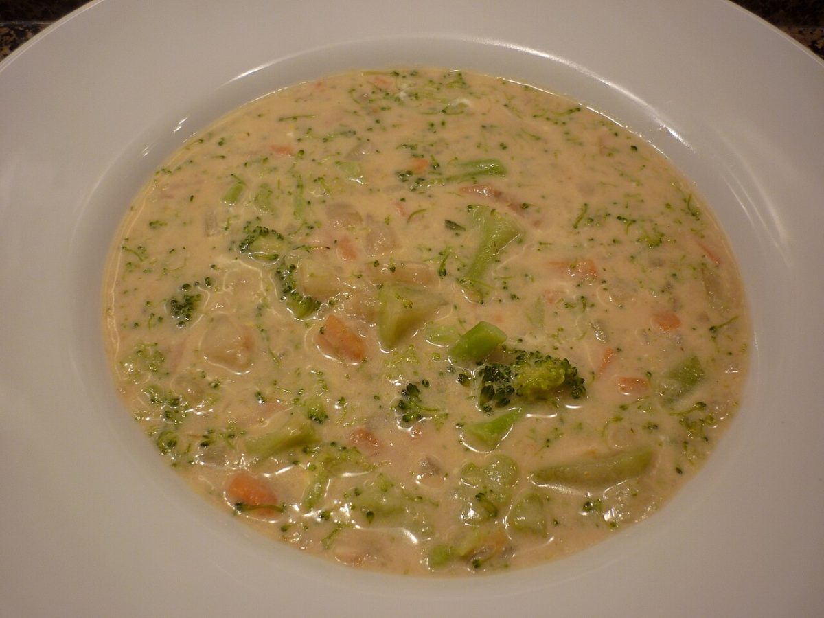 Creamy broccoli cheese soup with broccoli pieces and diced carrot in a wide white bowl