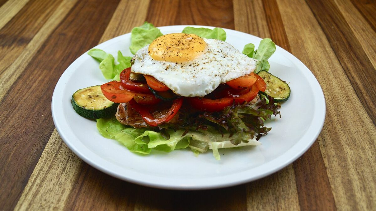 Bunless burger patty on lettuce with tomato, grilled zucchini and a fried egg on top