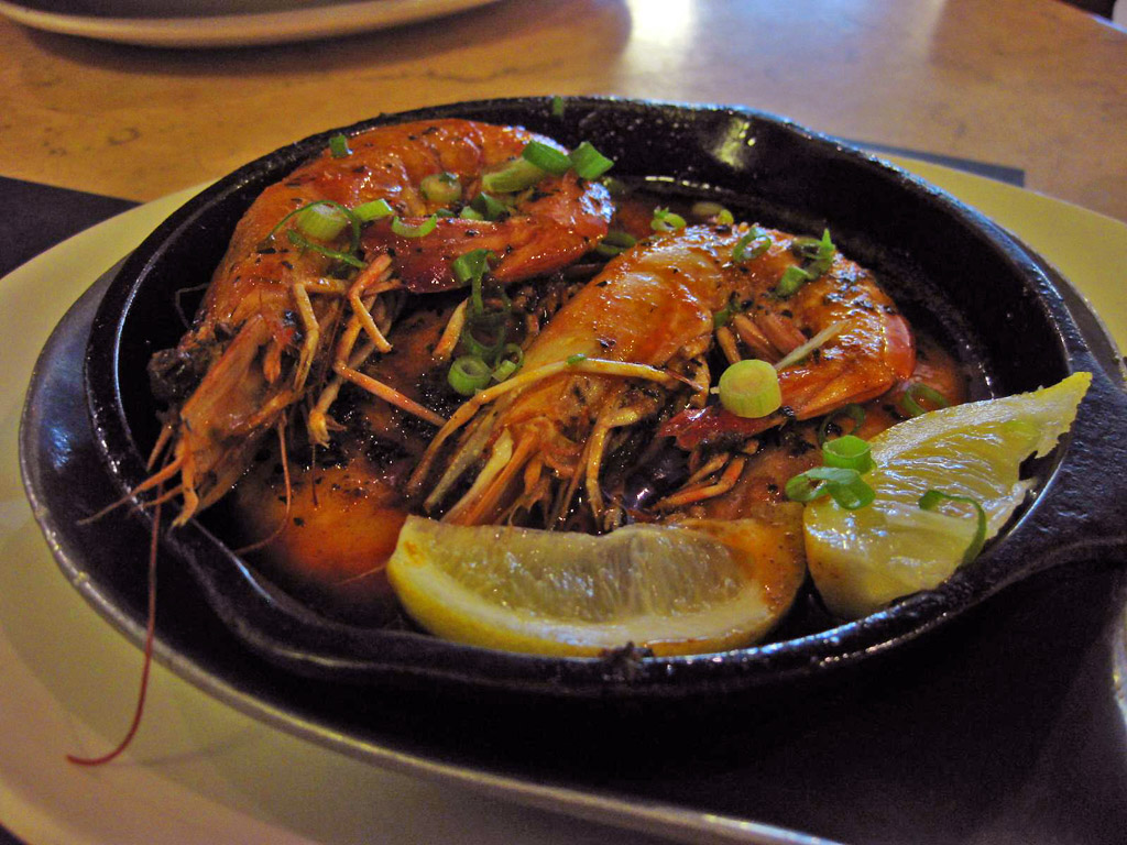 Blackened Cajun-spiced shrimp with green onions and lemon wedges in a small cast iron pan