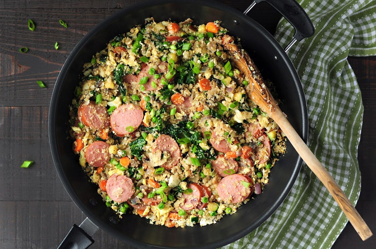 Cauliflower fried rice with sausage, egg, carrots, peas and green onion in a pan