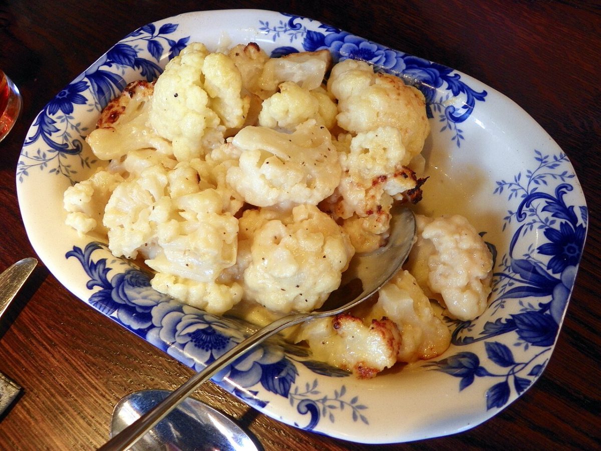 Baked cauliflower florets in a creamy cheese sauce on a blue and white platter