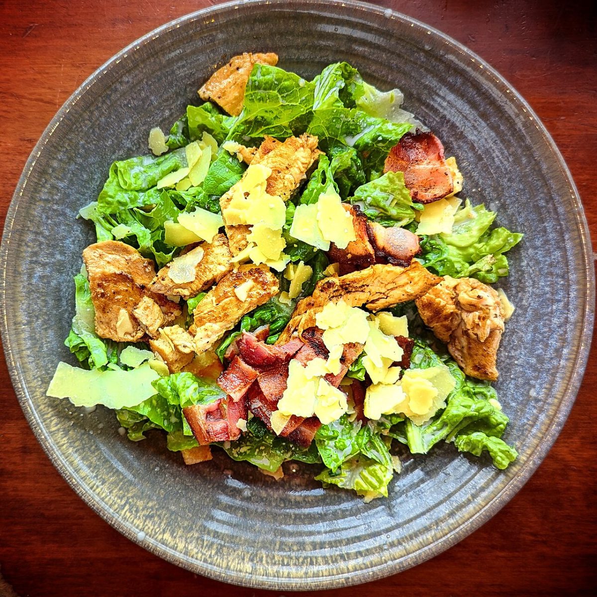 Chicken Caesar salad with romaine, bacon and shaved parmesan on a gray plate