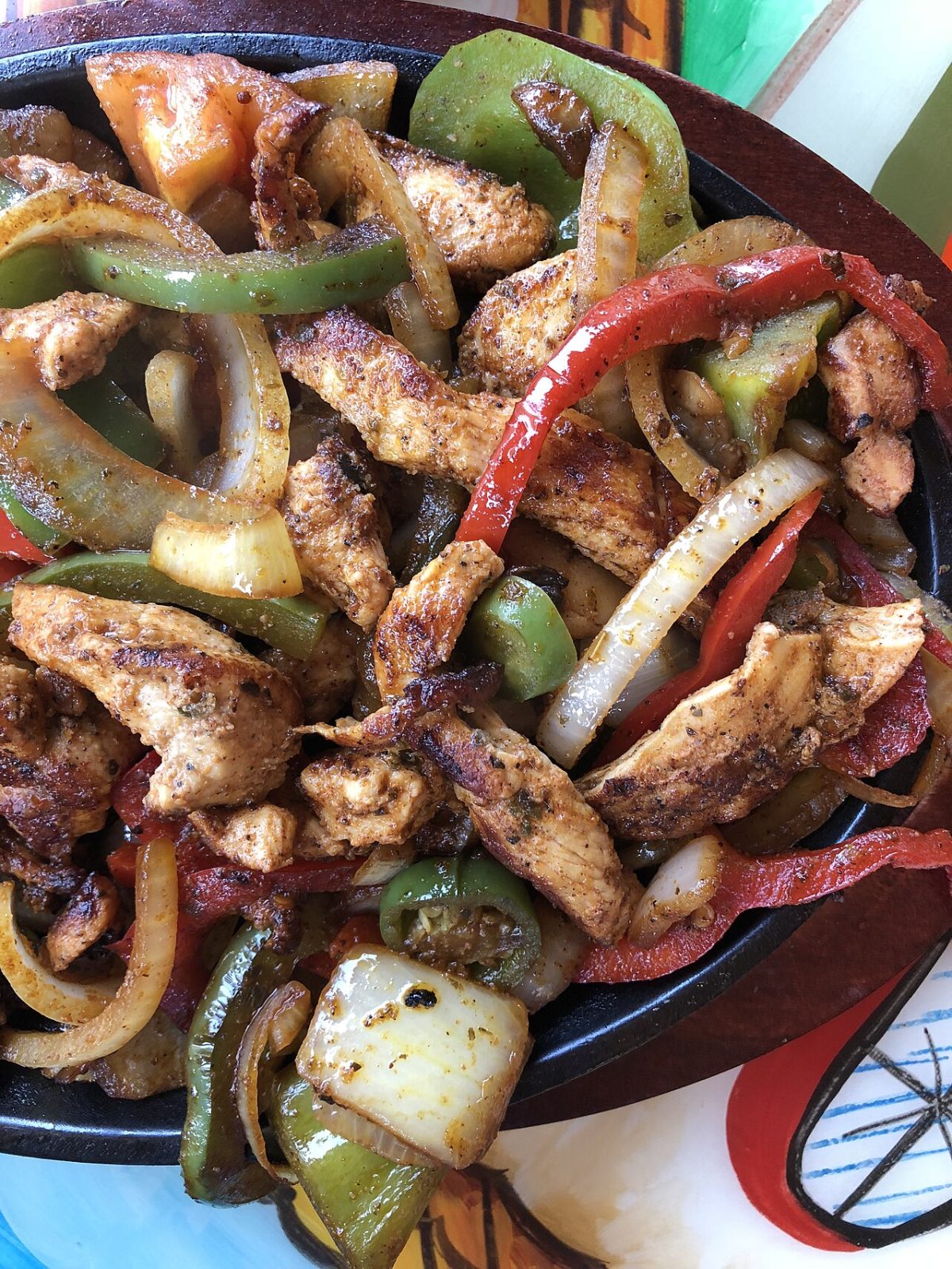 Seasoned chicken strips with red and green peppers and onions on a cast iron skillet