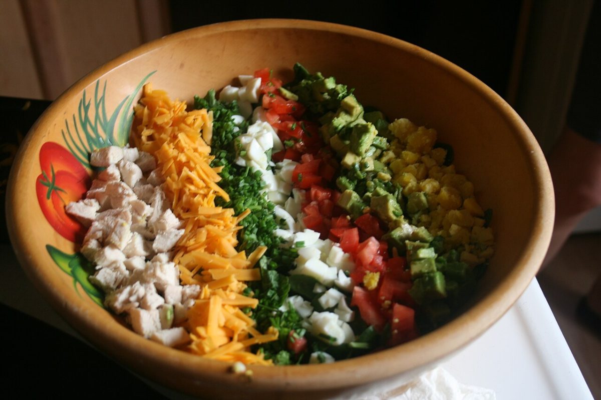 Cobb salad in a bowl with rows of chicken, cheddar, egg, tomato and avocado
