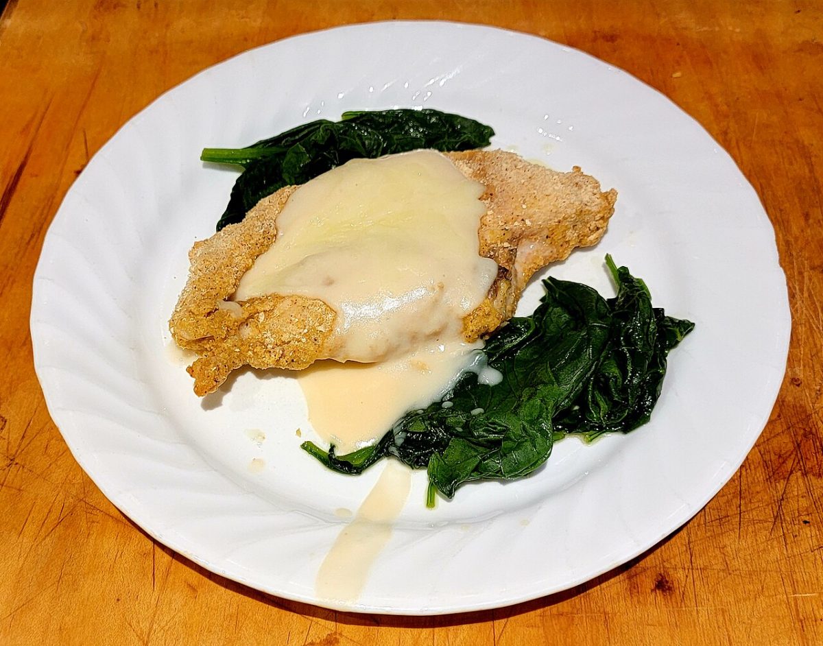 Chicken breast topped with creamy white sauce over wilted spinach on a white plate