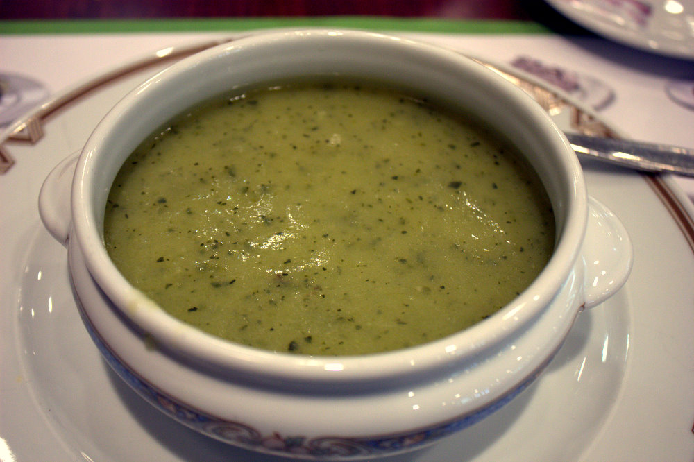 A bowl of smooth green zucchini soup on a saucer
