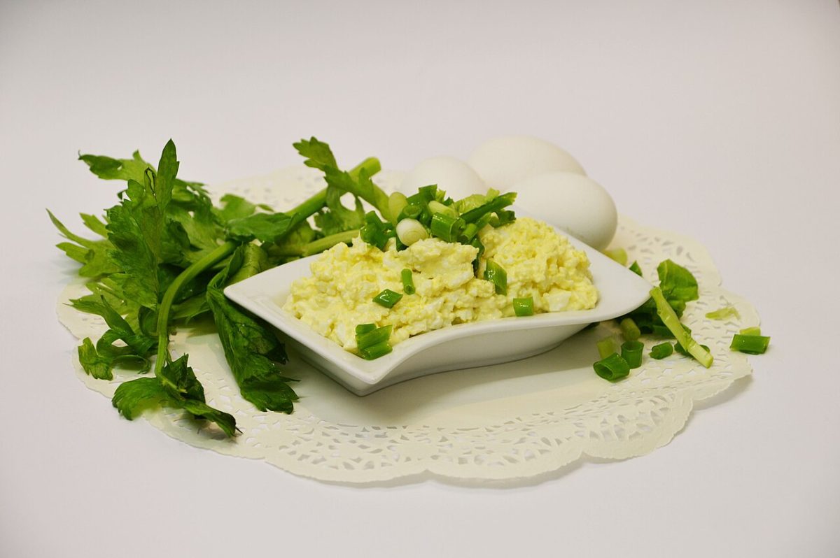Creamy egg salad with green onion in a white dish, with parsley and whole eggs
