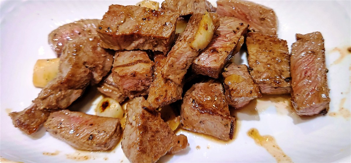 Seared cubes of steak with pan-fried garlic cloves on a white plate