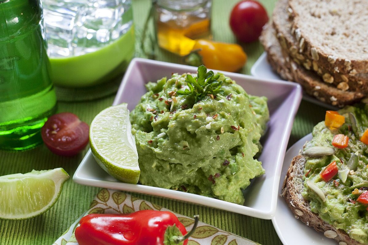Guacamole in a square bowl with lime wedges, cherry tomatoes and mini peppers