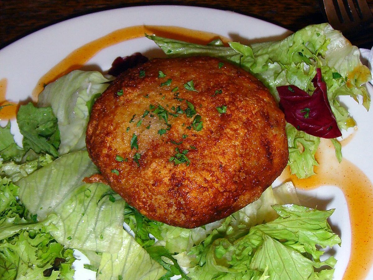 A golden salmon and cod fish cake with parsley on salad greens