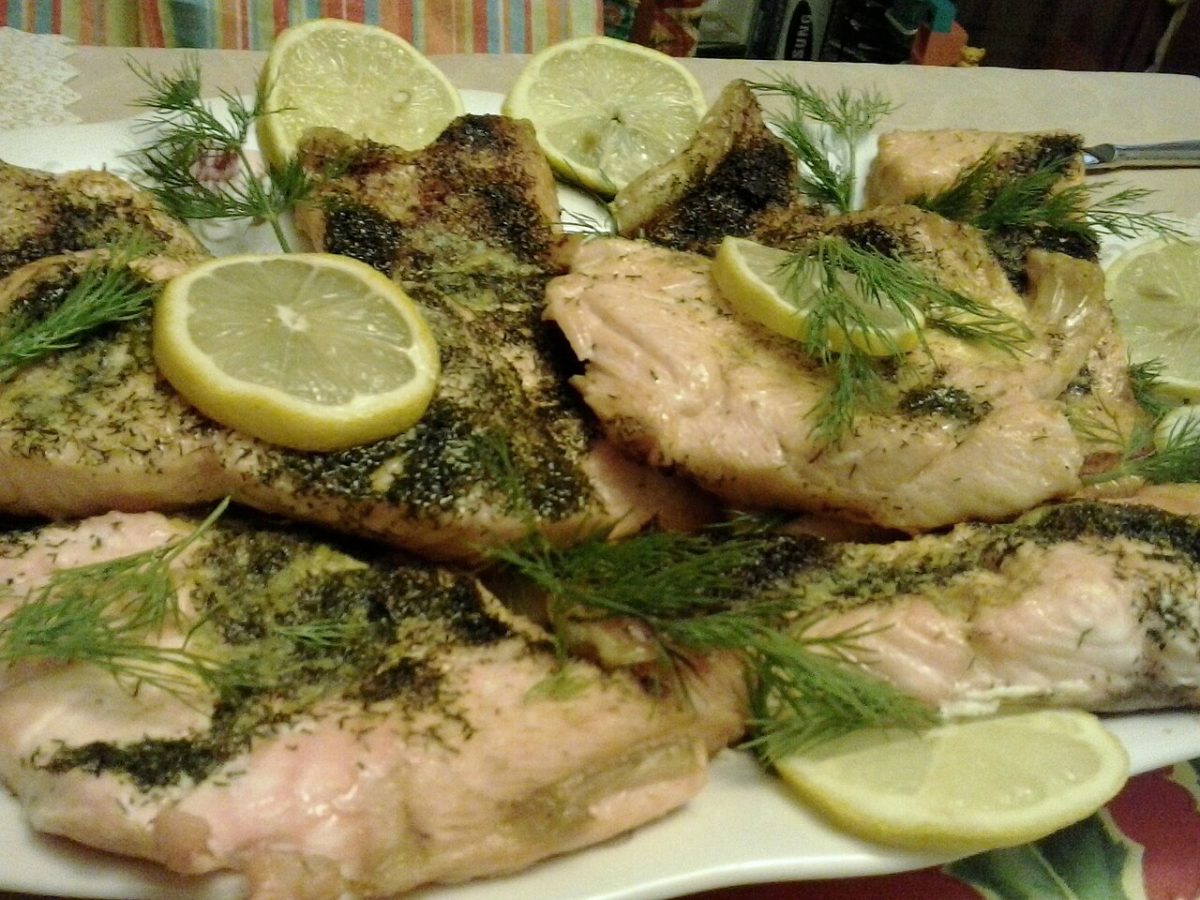 Baked salmon fillets topped with fresh dill and lemon slices on a platter