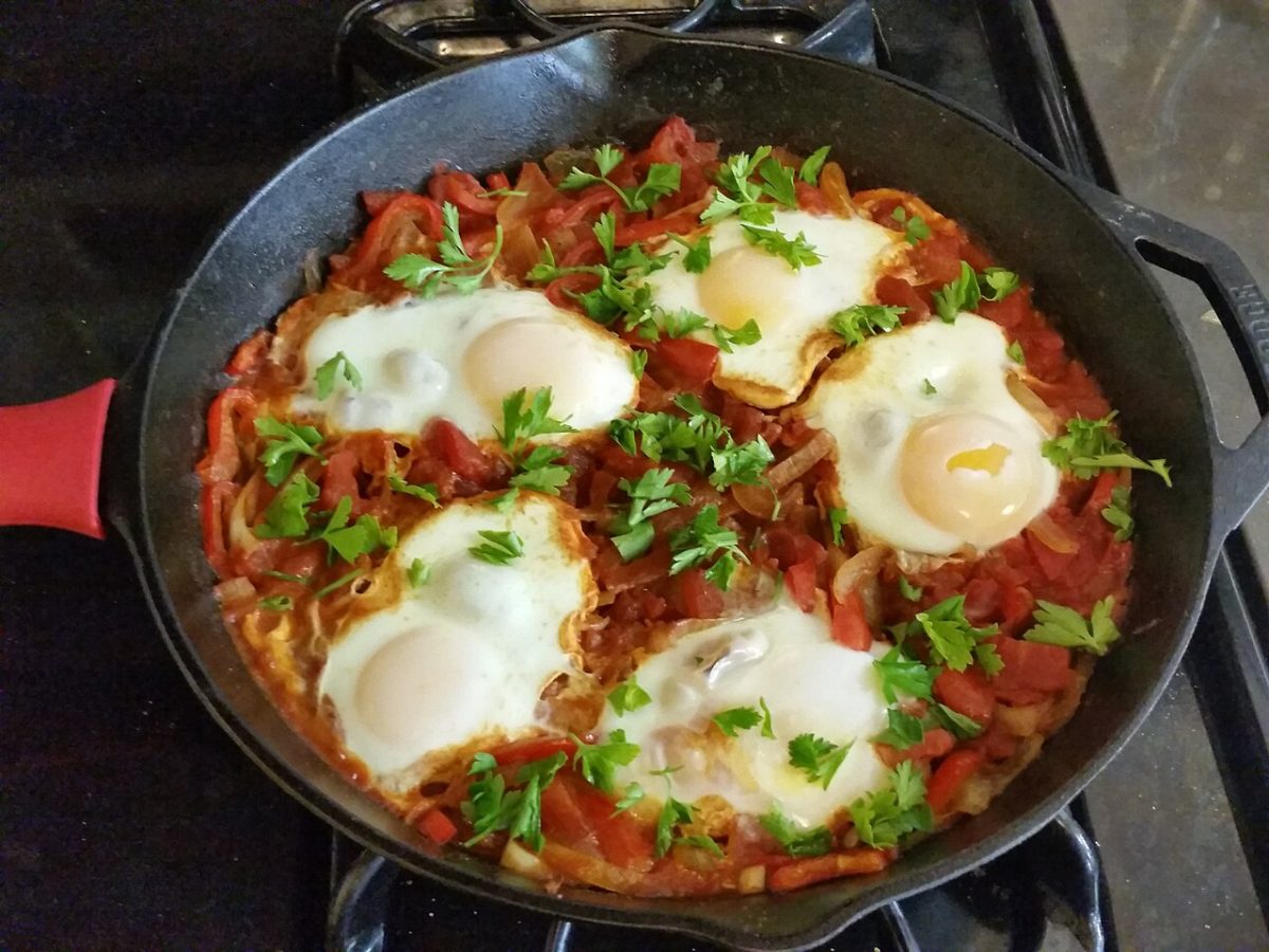 Eggs poached in tomato and pepper sauce in a cast iron skillet, topped with parsley