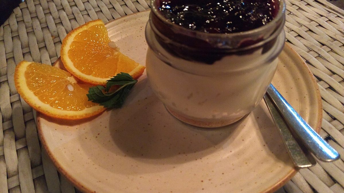 Cheesecake in a small glass jar topped with berry compote, with orange slices