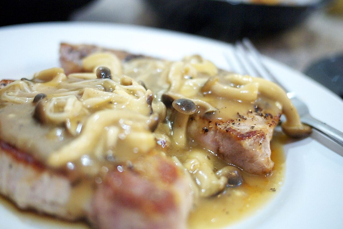 Seared pork chop covered in a creamy mushroom sauce with small brown mushrooms on a white plate