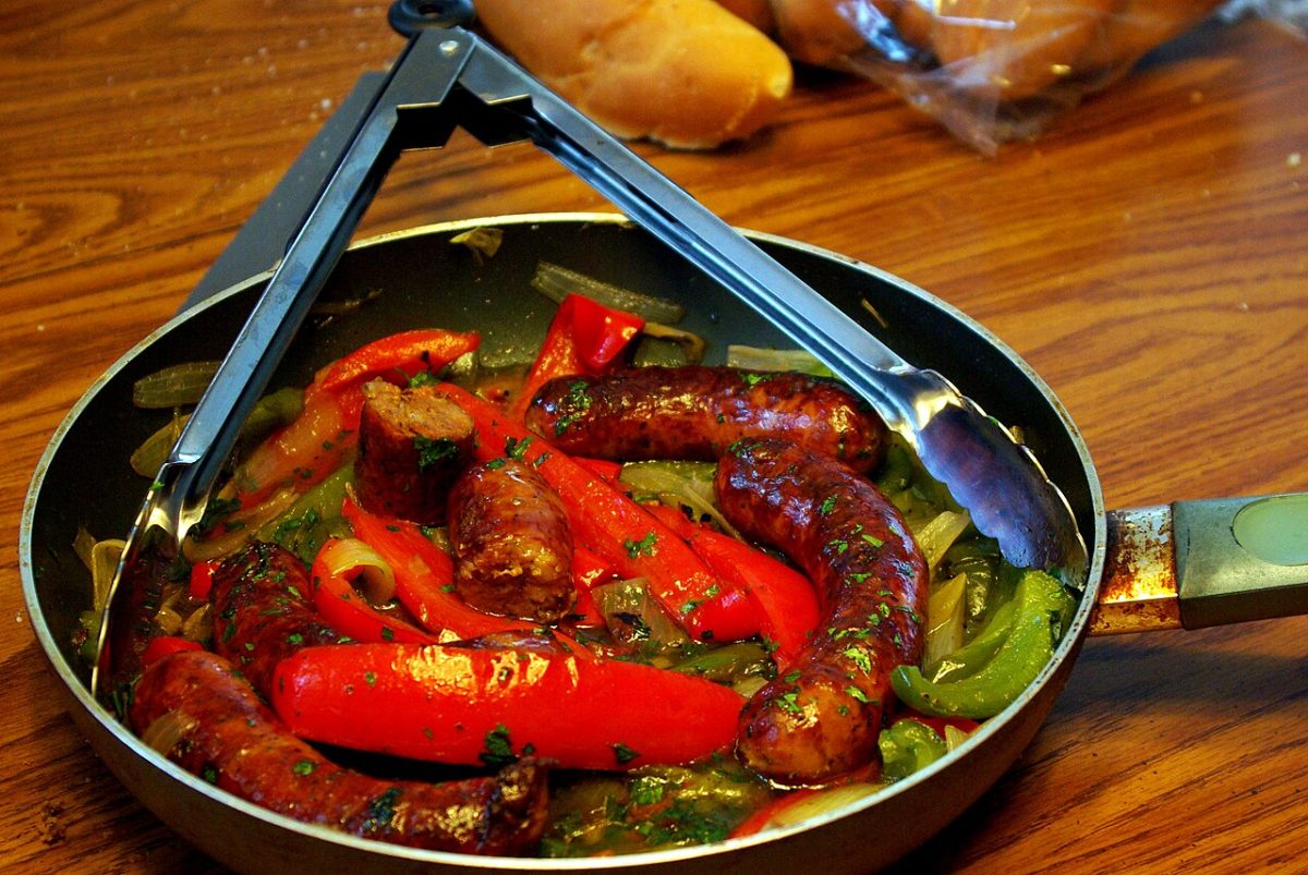 Browned sausages with red and green peppers in a skillet with tongs