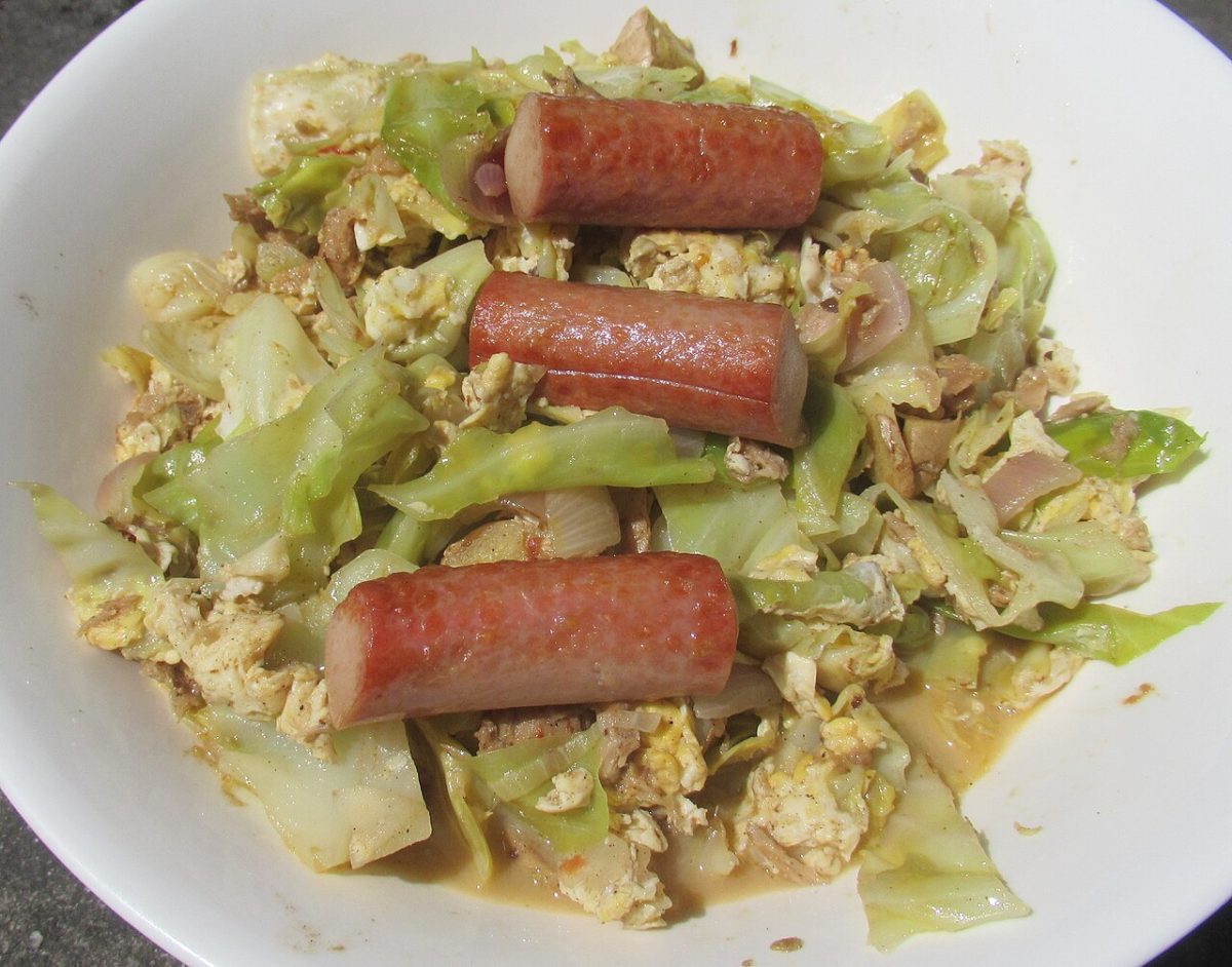 Fried cabbage with scrambled egg topped with pieces of smoked sausage in a white bowl