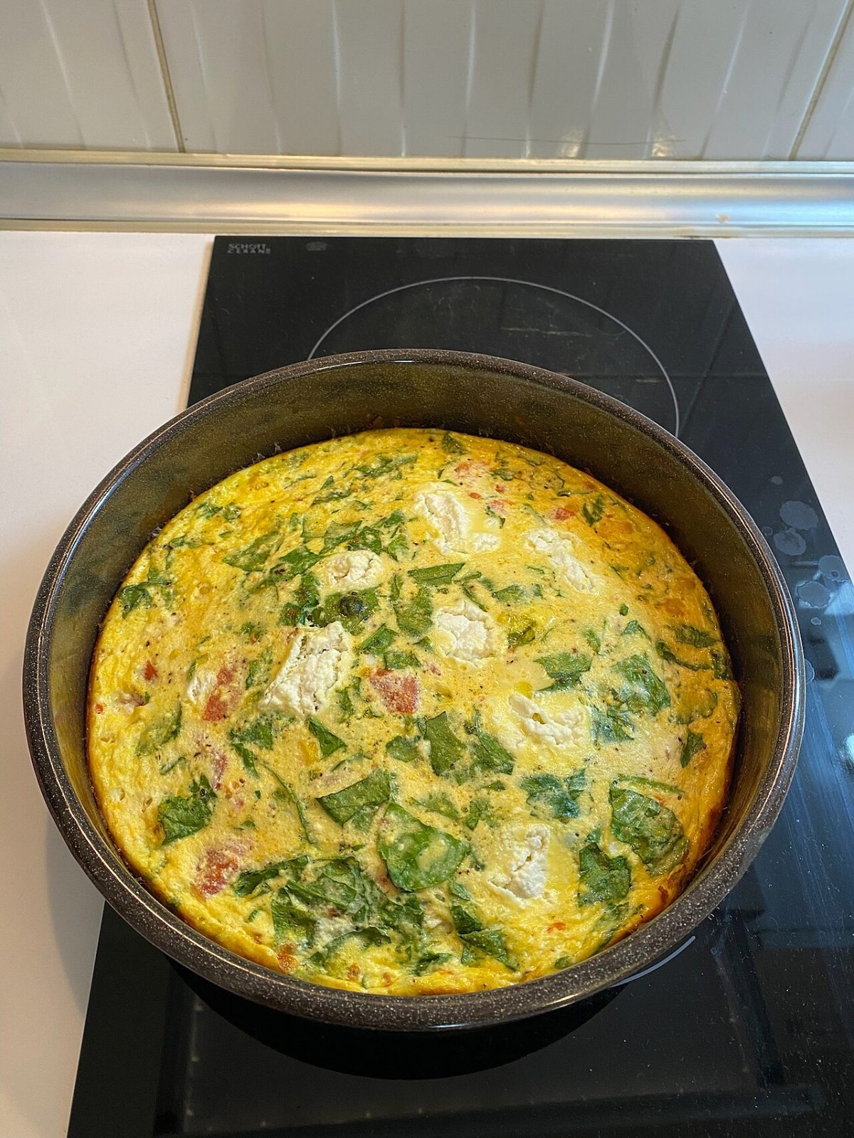 A baked egg frittata with spinach, crumbled feta and bits of red pepper in a round pan