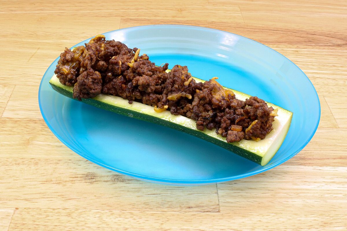 A halved zucchini topped with seasoned ground beef and cheese on a blue plate