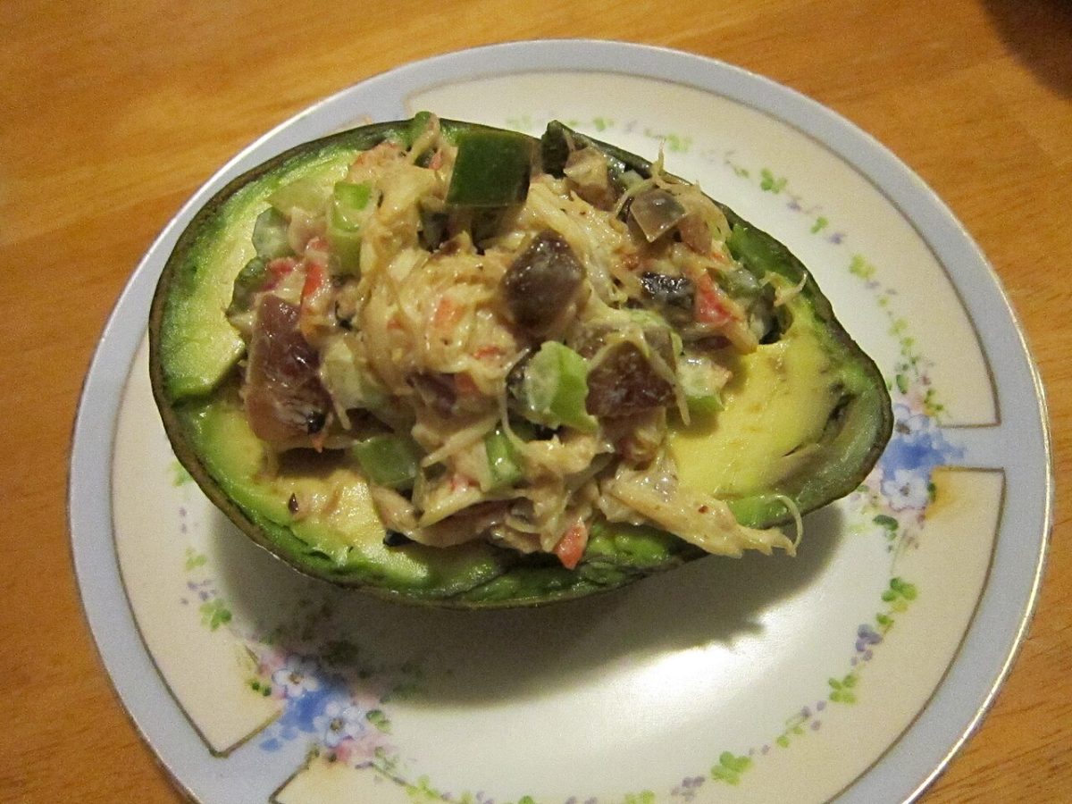 An avocado half filled with a creamy seafood and vegetable salad on a plate